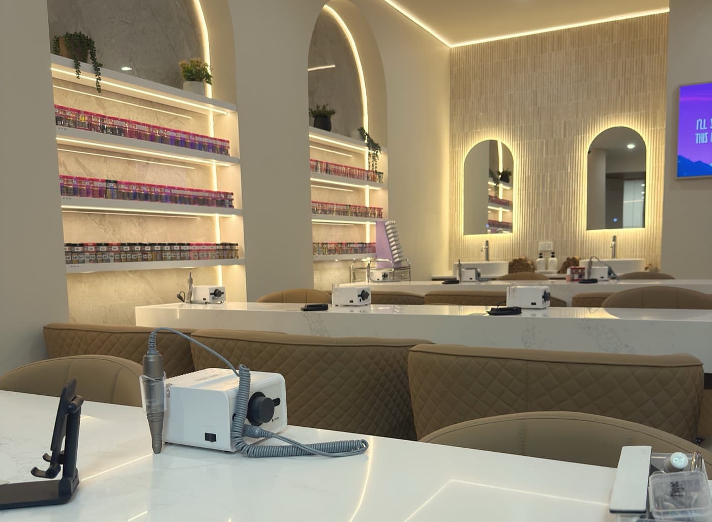 Manicure tables in white stone, with arched, back-lit shelves of polish behind